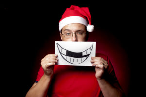 Man in santa hat covering mouth withdrawing of a smile with missing teeth